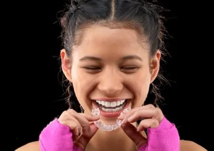 Teenage patient smiling while holding her Invisalign Teen aligner
